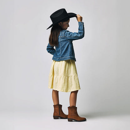 Niña con vestido amarillo y chamarra de mezclilla usando botines de piel Coqueta y Audaz en color miel.